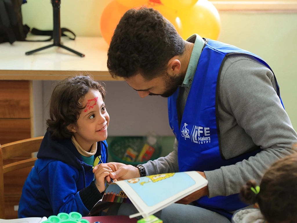 Adult helping a child read a picture book at a table