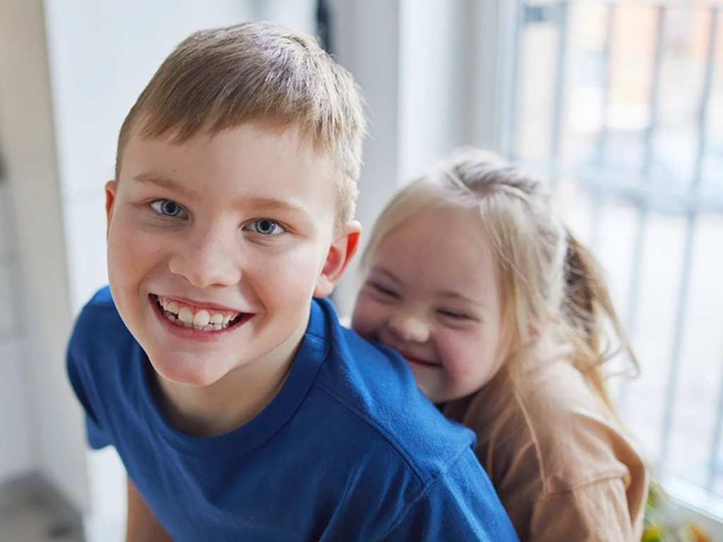 Two smiling children posing by a window